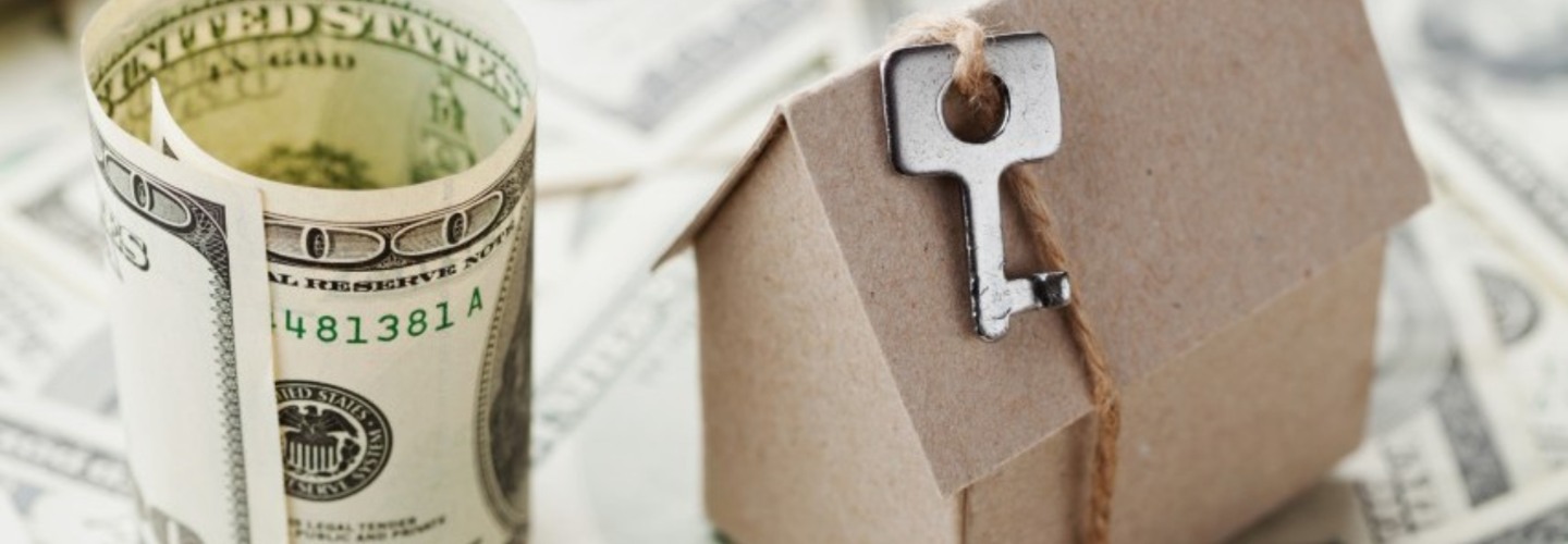 a small model house with a metal key next to a one hundred dollar bill